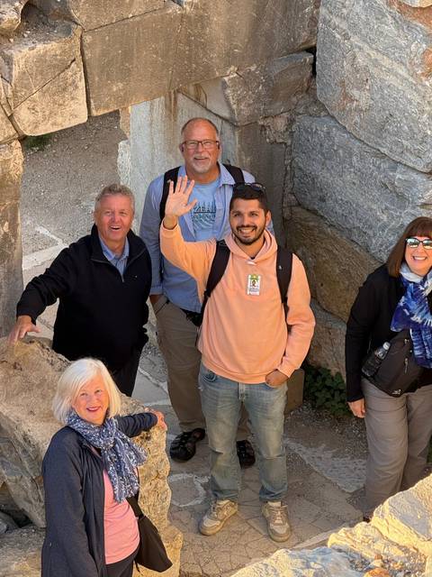 Group of people posing and waving among ancient stone ruins.