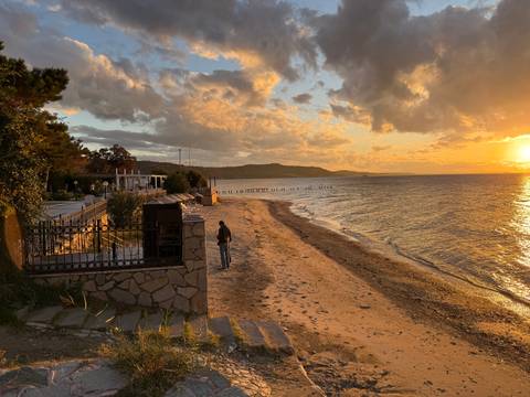 Sunset over a quiet sandy beach with one person walking along the shore.