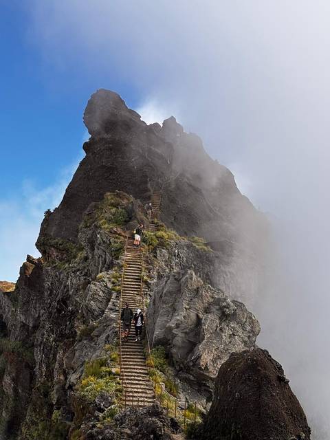 Narrow stairway on a rocky mountain peak with hikers ascending.