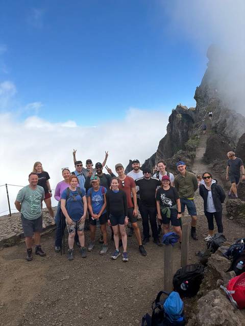 Group of hikers standing together on a mountain top with clouds below.