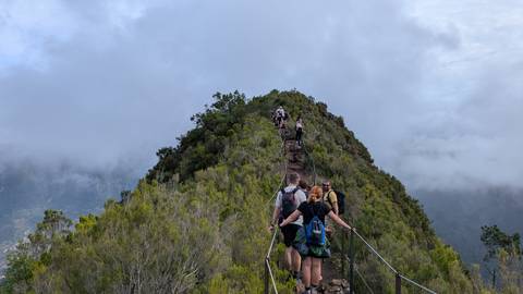 Hikers walking along a narrow mountain trail with clouds around.