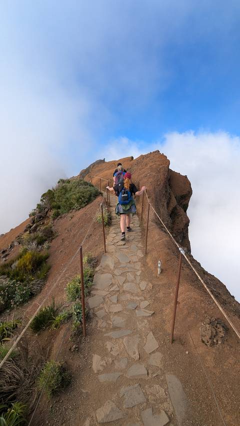 People hiking on a narrow mountain path.