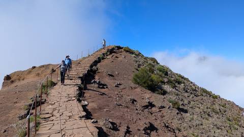 Hikers on a mountain path with clear blue skies.