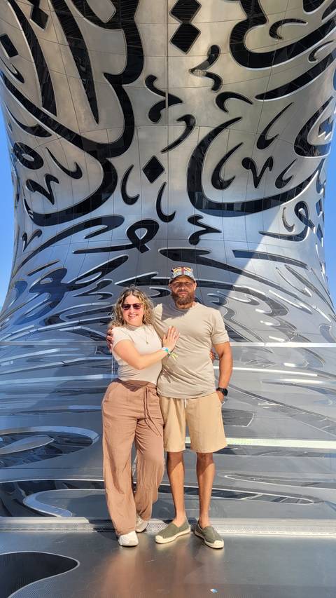 Two people stand in front of the facade with Arabic calligraphy.
