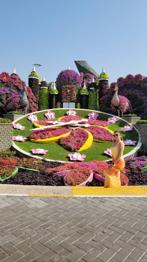 A woman posing in front of a floral clock with vibrant colors.