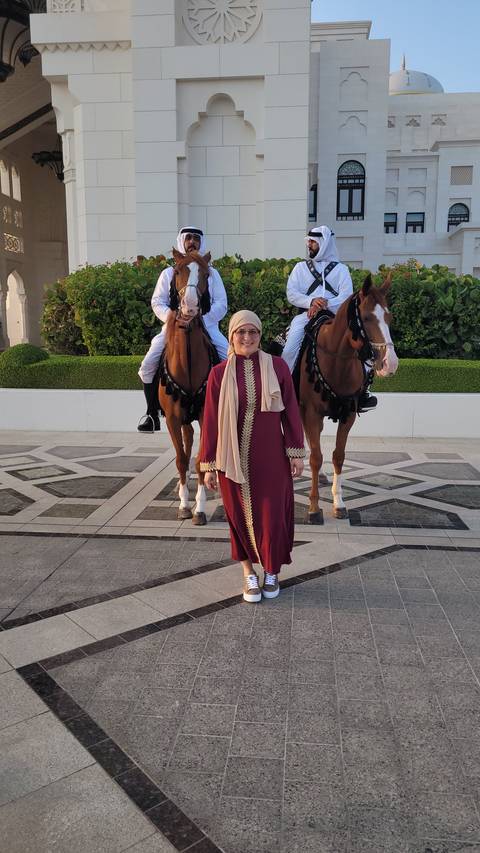 A woman stands in front of two mounted guards on horseback.
