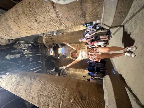 A woman posing joyfully under large inscriptions in an ancient structure.
