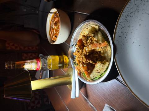 Indian food dish plated with a bottle of beer on a table.
