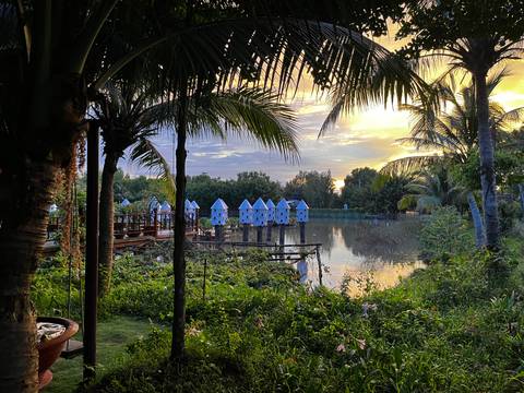 Scenic view of a lake surrounded by greenery and small huts at sunset.