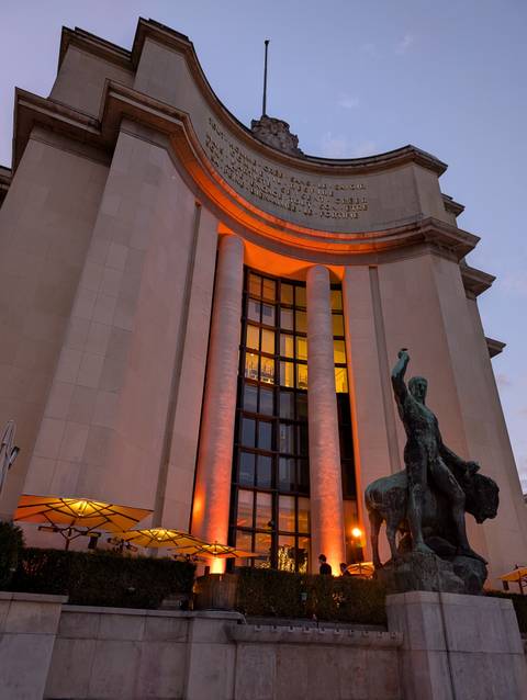 Statue and lighting decoration on a building facade at dusk.