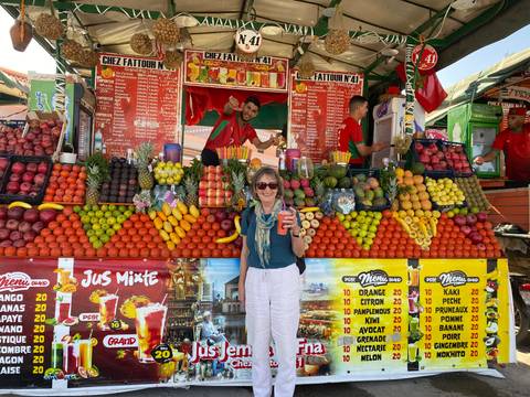 Woman holding a fruit drink in front of a colorful fruit stall.