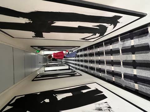 A person standing in a hotel hallway lined with artwork.