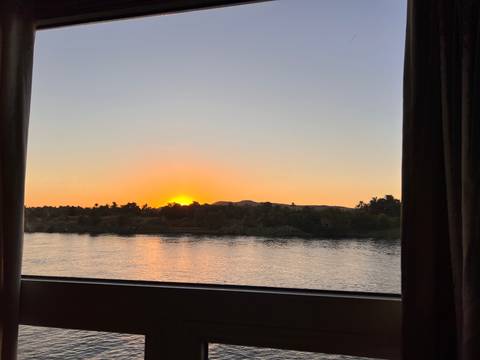 Scenic river view from a window at sunset with silhouettes of trees.