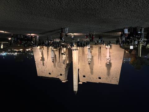 Night view of a grand Egyptian temple with tourists gathered.