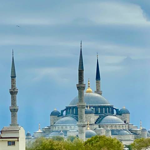 Top of a mosque with minarets against cloudy sky.