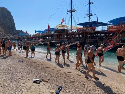 People enjoying the beach near tour boats.