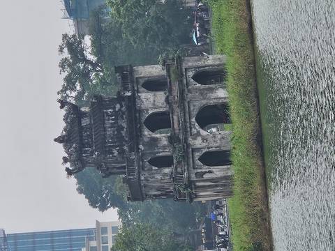 Large tower in the middle of a lake surrounded by greenery.