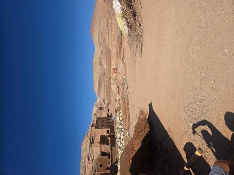 A barren, desert landscape with a small settlement and mountains in the background.