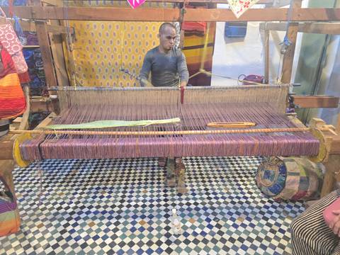 A person operating a large traditional loom with colorful textile.