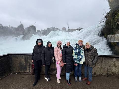 A group of women posing in front of a large waterfall.