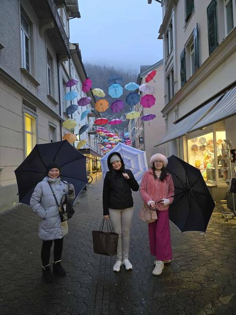 Three women with umbrellas in a colorful street with hanging umbrellas.