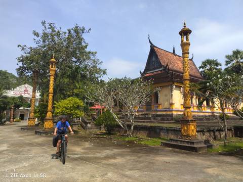 A person on a bicycle passing a temple.