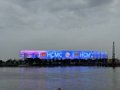 Digital billboard saying 'I ❤️ HCMC' near a water body.
