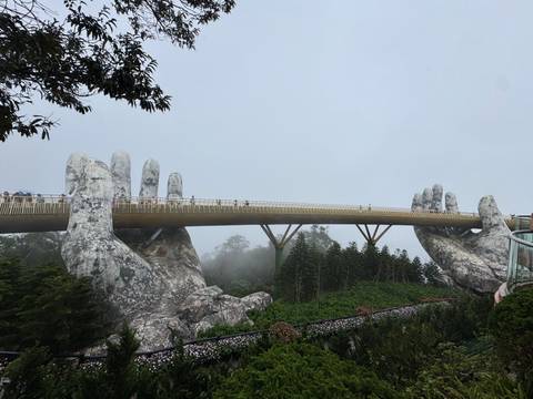 Large hands sculpture holding a pedestrian bridge amidst mist.