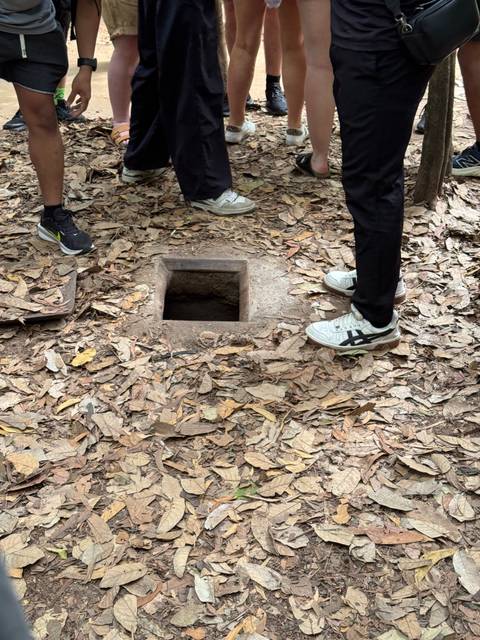 Concrete tunnel entrance surrounded by foliage, with people's feet visible.