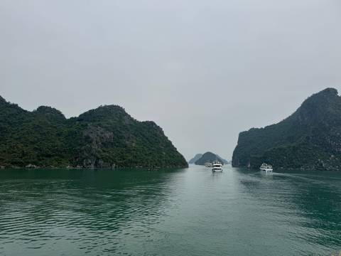 Narrow passage between limestone islands with boats under a cloudy sky.