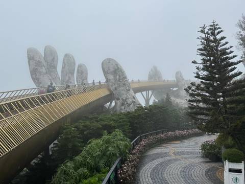 Misty view of the Golden Bridge held by giant hands in a garden.