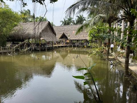 Traditional thatched-roof huts on stilts over water surrounded by greenery.