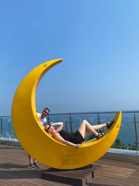 Person playfully posing on a large yellow crescent structure.