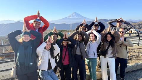 A group of people making a gesture in front of a mountain, possibly Mount Fuji.