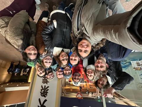 A large group selfie with people smiling indoors.