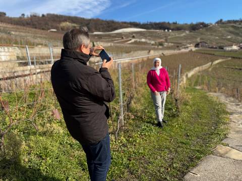 Man taking a picture of a woman in a vineyard.