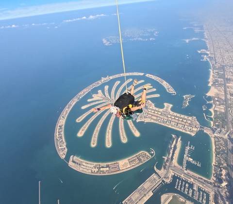 Skydivers over a Palm-shaped island in clear blue waters.