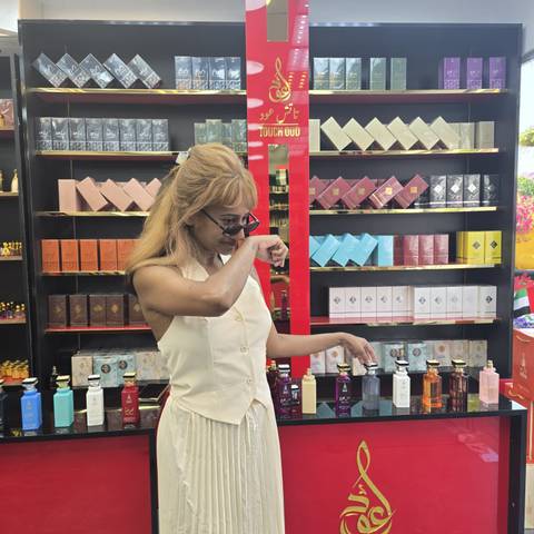 Woman smelling perfumes in a shop with lined shelves behind her.