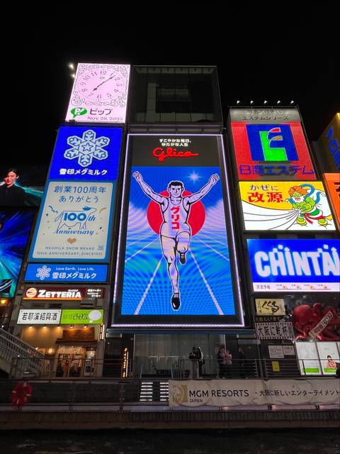 Brightly lit advertisement signs in an urban setting at night.