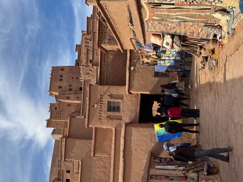 Market street in a historic Moroccan town with locals and tourists.