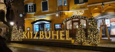 Kitzbühel sign with decorative lights on a building facade.