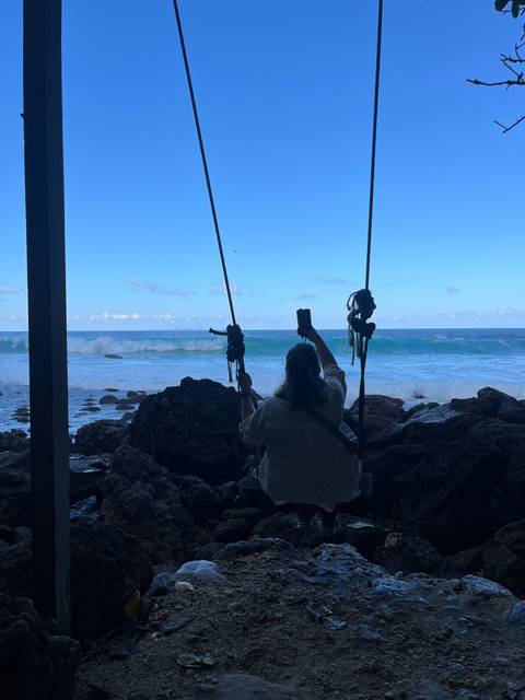 Person on a swing taking a photo with the ocean in the background.