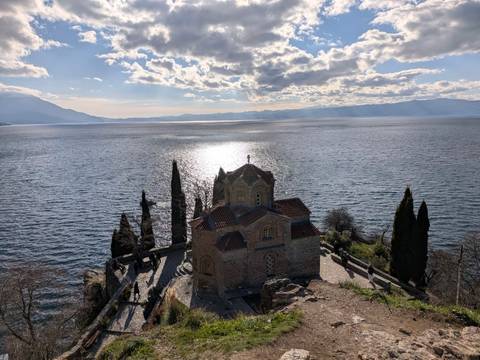 Church on a cliff overlooking a large lake with mountains.