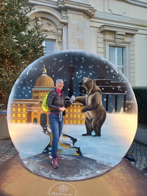 Person posing with a bear statue in a snow globe.