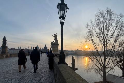 Sunset view of Charles Bridge in Prague with walking pedestrians.