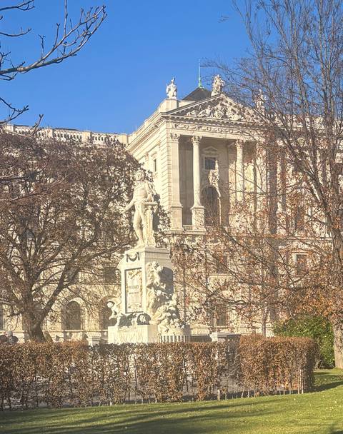Statue in front of a large building with trees.