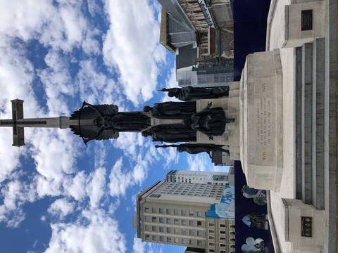 War memorial with statues and tall, historic buildings in the background.