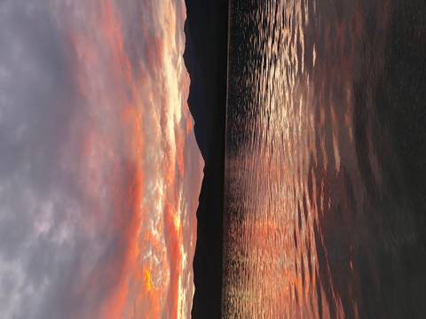 Dramatic sunset reflecting on a lake with mountain silhouettes.