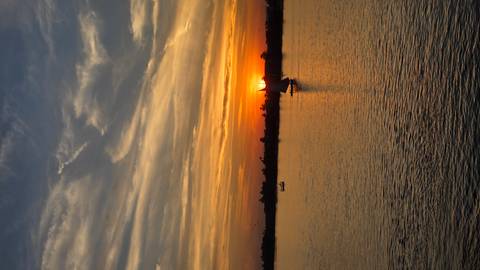 Sailboat on a river at sunset with a warm sky.