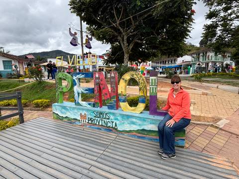Woman sitting by a sign in a colorful town.